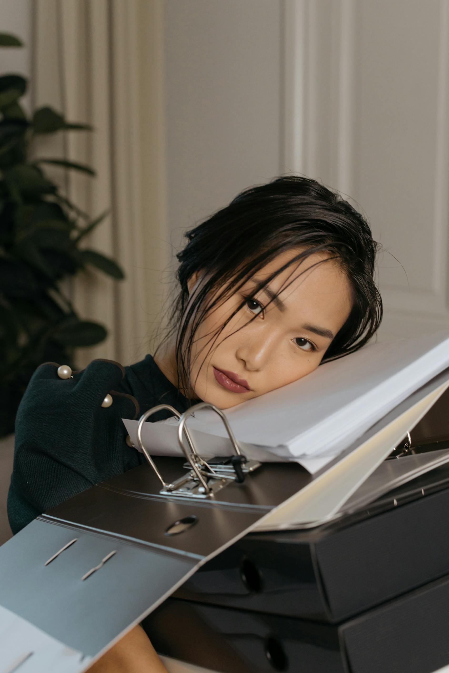 Asian woman resting on a stack of office folders, showcasing work fatigue and stress.